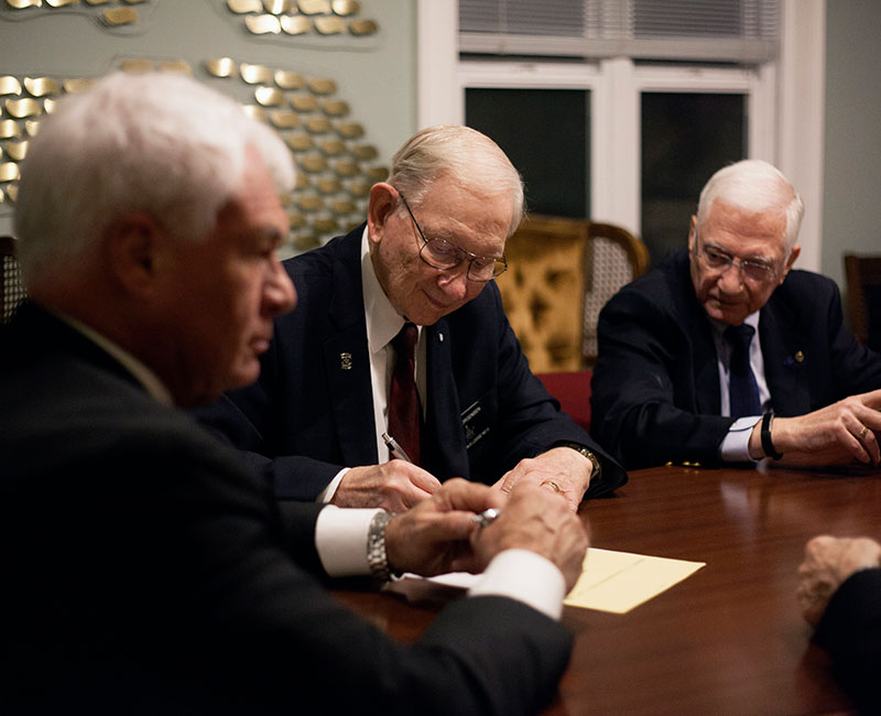 Three older gentlemen sign documents in a meeting room